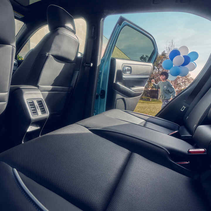 Primer plano del asiento trasero del Honda e:Ny1 con un niño que pasa junto a la puerta abierta con globos.