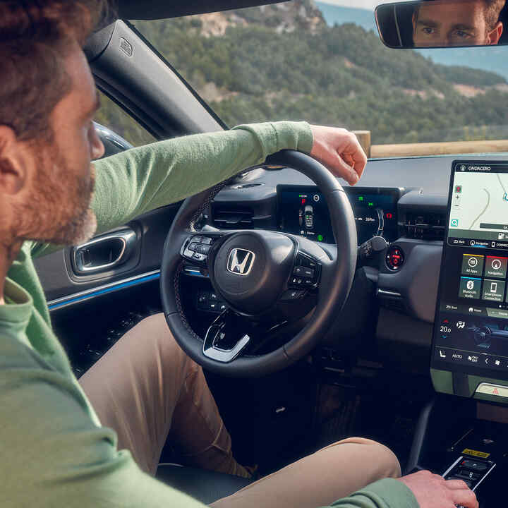 Hombre conduciendo un Honda e:Ny1 usando la navegación en la pantalla digital del conductor.